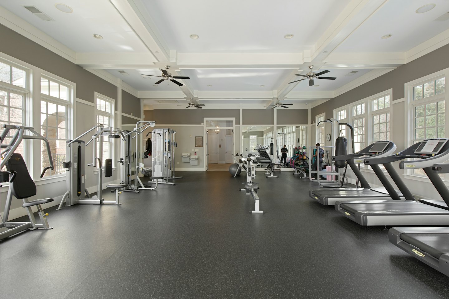 Fitnessstudio mit Hantelgeräten und Laufbändern auf Gummiboden.